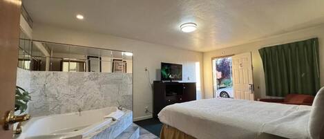 Habitación de hotel con una cama grande, una bañera, un televisor y vistas al exterior.