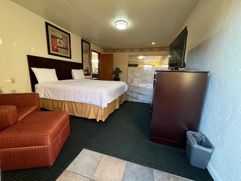 A hotel room with a bed, a desk, a chair, a trash bin, and a television.
