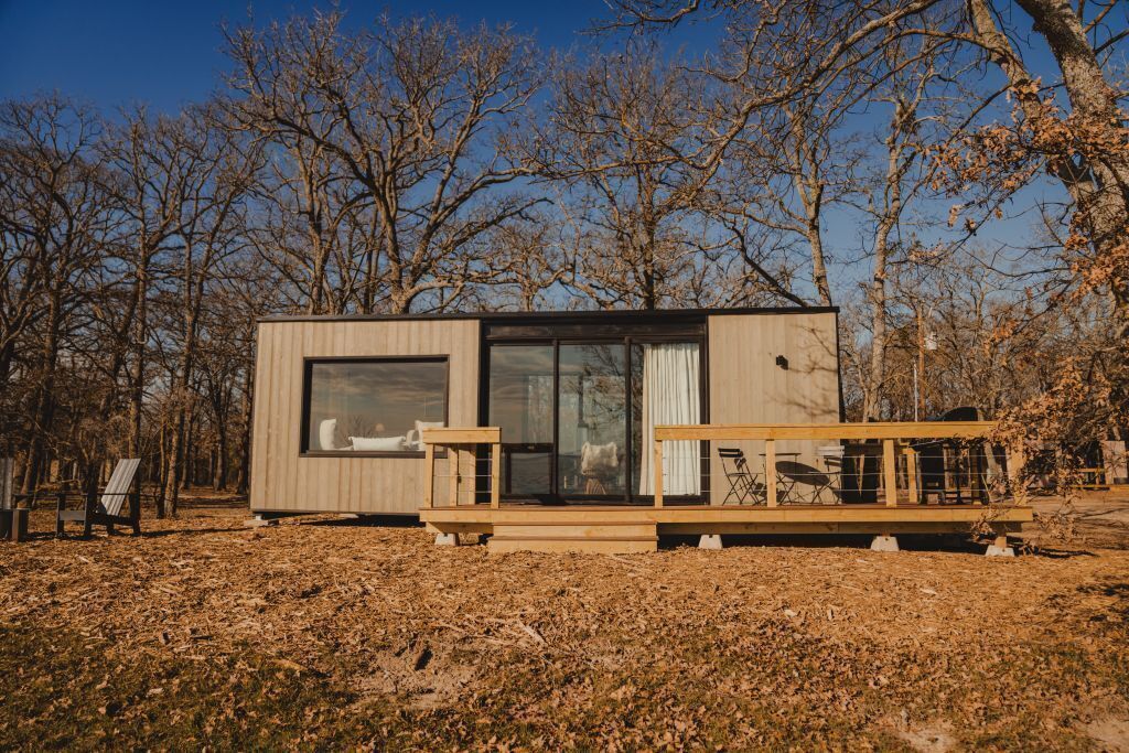 A modern cabin with large windows, a deck, and a view of the surrounding trees.
