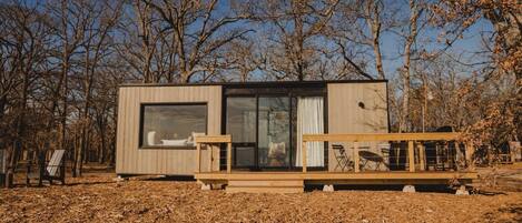 A modern cabin with large windows, a deck, and a view of the surrounding trees.