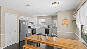 Una cocina moderna con armarios blancos, una mesa de comedor de madera y una lámpara en el techo.