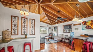 A spacious kitchen with a wooden ceiling, a dining area with red stools, and a living room with a sofa and a painting of a cow. - Mountain Treehouse - Magpie Nest (Mentone)