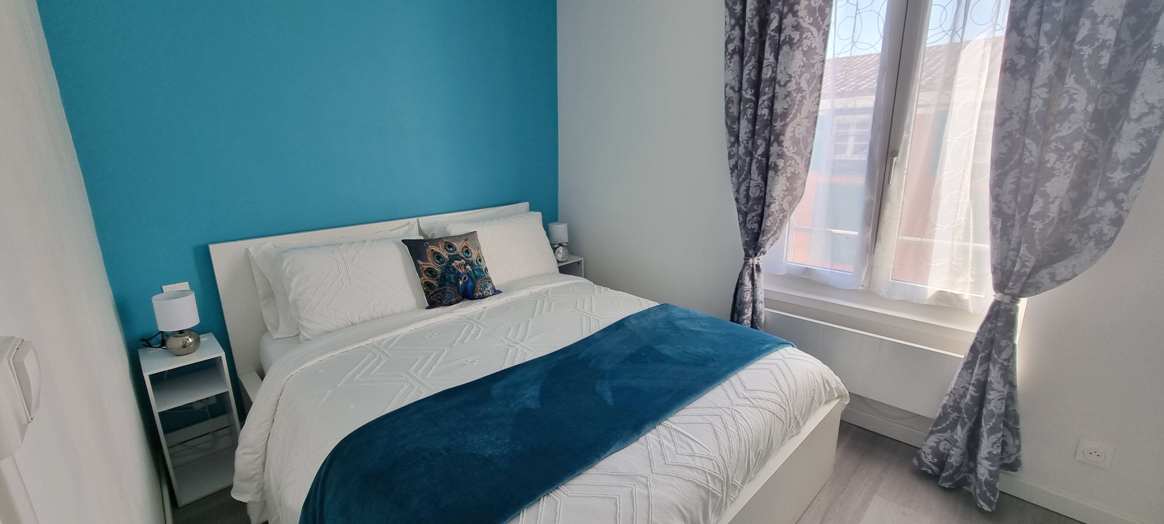 A bedroom with a bed, a nightstand, a lamp, and a window with curtains.