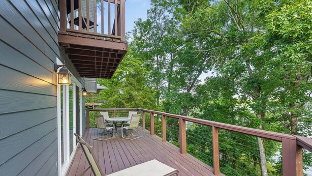 A wooden deck with a table and chairs, overlooking a forested area.