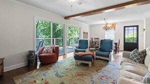 A spacious living room with a large window, a ceiling fan, and a variety of seating options including a red armchair, a blue armchair, and a beige sofa.