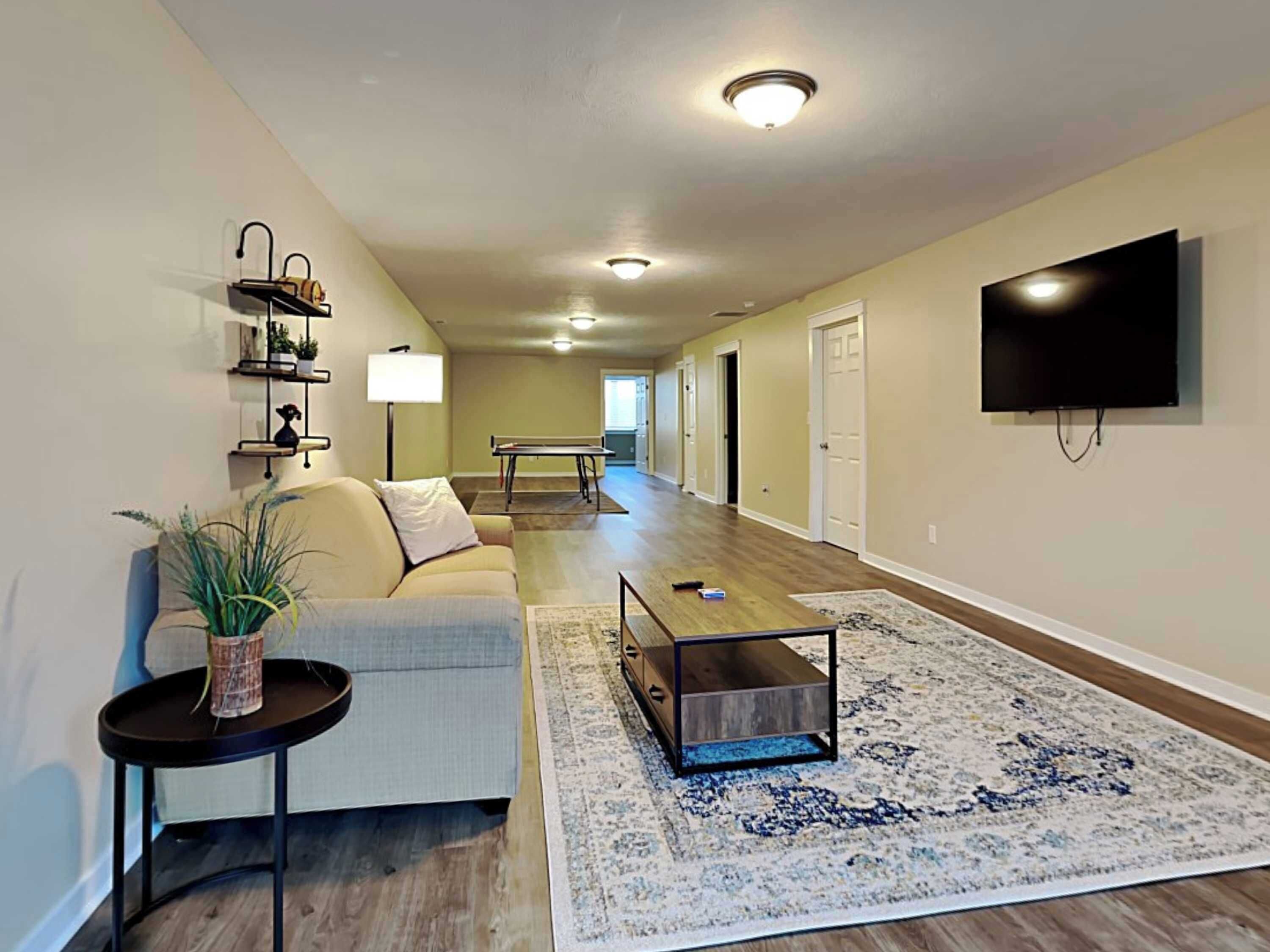 A spacious living room with a sofa, coffee table, and a flat-screen TV mounted on the wall.