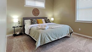 A bedroom with a large bed, two bedside tables with lamps, a wall clock, and a decorative wall piece.