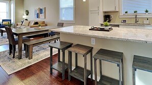 A modern kitchen with a central island, bar stools, and a dining area with a sofa and coffee table.