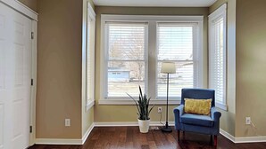 A room with hardwood flooring, a blue armchair with a yellow pillow, a floor lamp, and a potted plant.