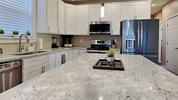 A modern kitchen with white cabinets, stainless steel appliances, and a granite countertop.