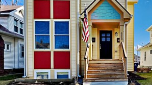 A two-story house with a red and beige color scheme, a front porch, and an American flag.