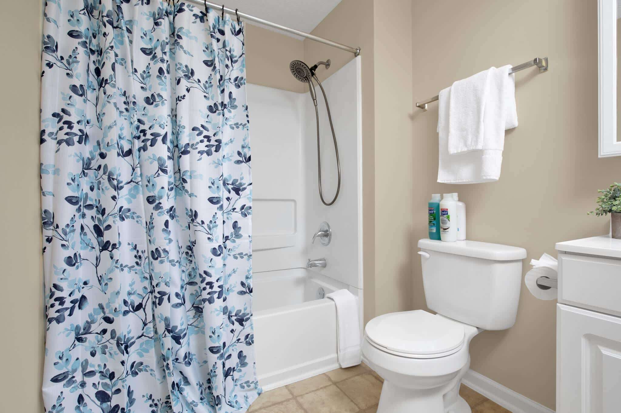A bathroom with a shower curtain, a bathtub, a toilet, and a towel rack.