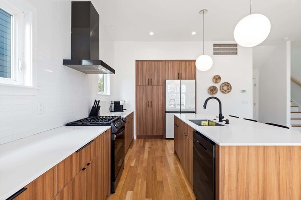 A modern kitchen with white countertops, wooden cabinets, a black stove, and a central island with a sink. - Modern Amenities, Downtown - Raleigh Craftsman (Raleigh)