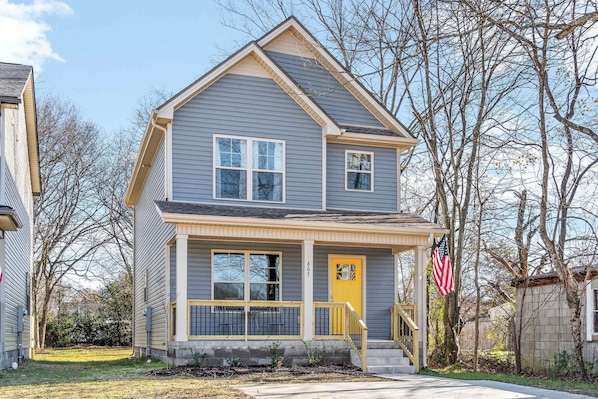 A two-story house with a front porch, a yellow door, and an American flag.