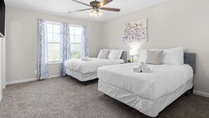 A hotel room with two beds, a ceiling fan, a window with patterned curtains, and a wall-mounted artwork.