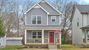 A two-story house with a red door, a small porch, and an American flag.