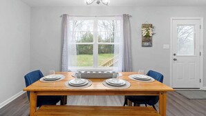 A dining area with a wooden table set for four, a chandelier, and a view of a garden through a large window.