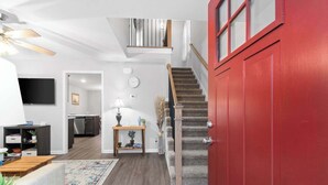 A modern living room with a staircase, a kitchen, and a dining area.