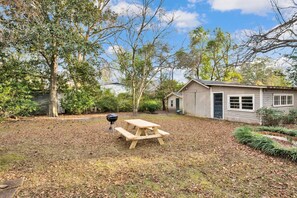Un jardin avec une table de pique-nique, un barbecue et un petit abri de jardin.