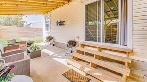 A covered patio with outdoor furniture, a barbecue grill, and a large window.