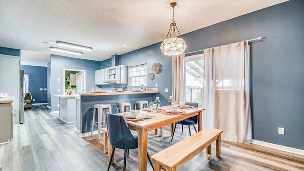 A modern kitchen with a central island, a dining area with a wooden table and benches, and a large window with curtains.
