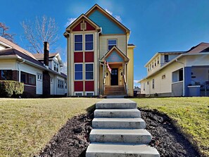 Une maison à deux étages avec un porche à l’avant et un petit jardin devant.