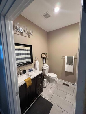 Une salle de bain avec un lavabo blanc, des meubles sombres, des toilettes et un espace douche.