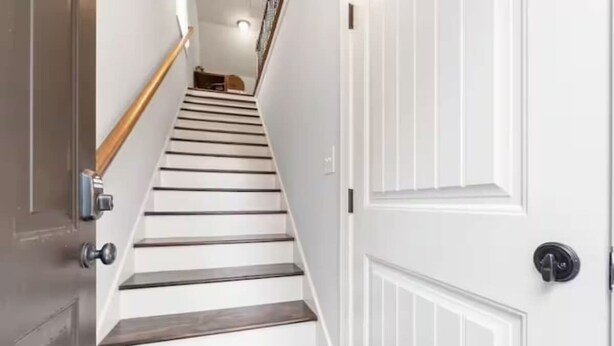 A staircase with wooden steps and white walls, leading to a door with a round handle.