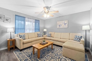 A living room with a beige sectional sofa, a wooden coffee table, a patterned rug, a ceiling fan, and two floor lamps. - 1-Mile to Downtown Clarksville! Queen-City Comfort (Clarksville)