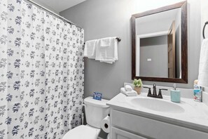 A bathroom with a shower curtain, a toilet, a sink with a mirror, and a small potted plant.