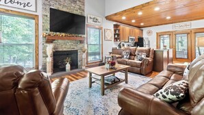 A spacious living room with leather sofas, a fireplace, wooden beams, and a kitchen area. - Updated Cabin - Hiwassee Highlife (Decatur)