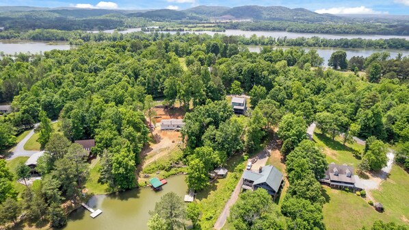 An aerial view of a residential area with houses surrounded by dense greenery and a lake in the background. - Updated Cabin - Hiwassee Highlife (Decatur)