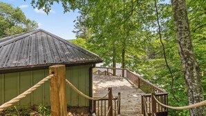 A wooden cabin with a metal roof, surrounded by trees and a wooden walkway leading to it. - Updated Cabin - Hiwassee Highlife (Decatur)