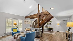 Amplia sala de estar con una escalera de madera, un sofá gris, sillones azules y una mesa de centro.