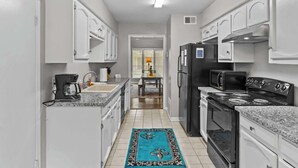 Una cocina estrecha con gabinetes blancos, un refrigerador negro, una estufa y un microondas.