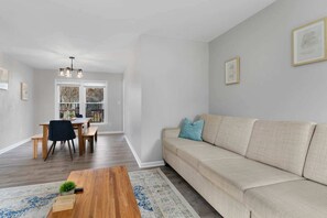 A living room with a sofa, a coffee table, a dining table with chairs, and a chandelier.