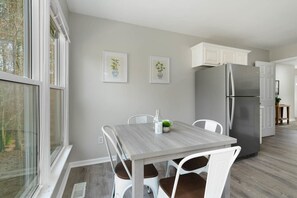 Una cocina moderna con un refrigerador grande, armarios blancos y una mesa de comedor con sillas.