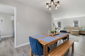 A dining area with a wooden table, chairs, and a bench. There is a sofa and a window in the background. - Near NC State Campus & Downtown - The Maple Marvel (Raleigh)