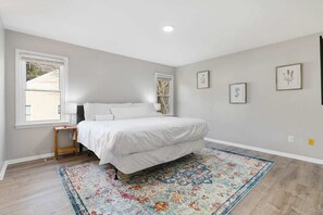A bedroom with a bed, a window, a small table, and a rug.