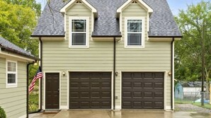 A two-story house with a gabled roof, two garage doors, and an American flag on the left side.
