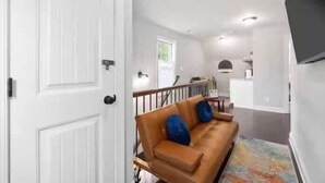 A hallway with a white door, a brown sofa with blue cushions, and a painting on the wall.