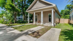 A single-story house with a covered porch, a front yard with a lawn and a concrete pathway, and a wooden fence in the background. - Near Downtown, Dining & Base - Beach Flow Bungalow (Pensacola)