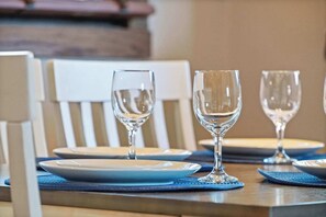 Una mesa de comedor dispuesta con platos y copas de vino, rodeada de sillas.
