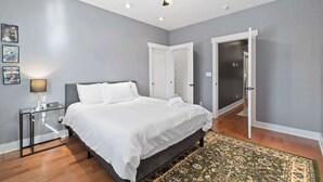 A bedroom with a bed, a nightstand, a lamp, a ceiling fan, and a door.