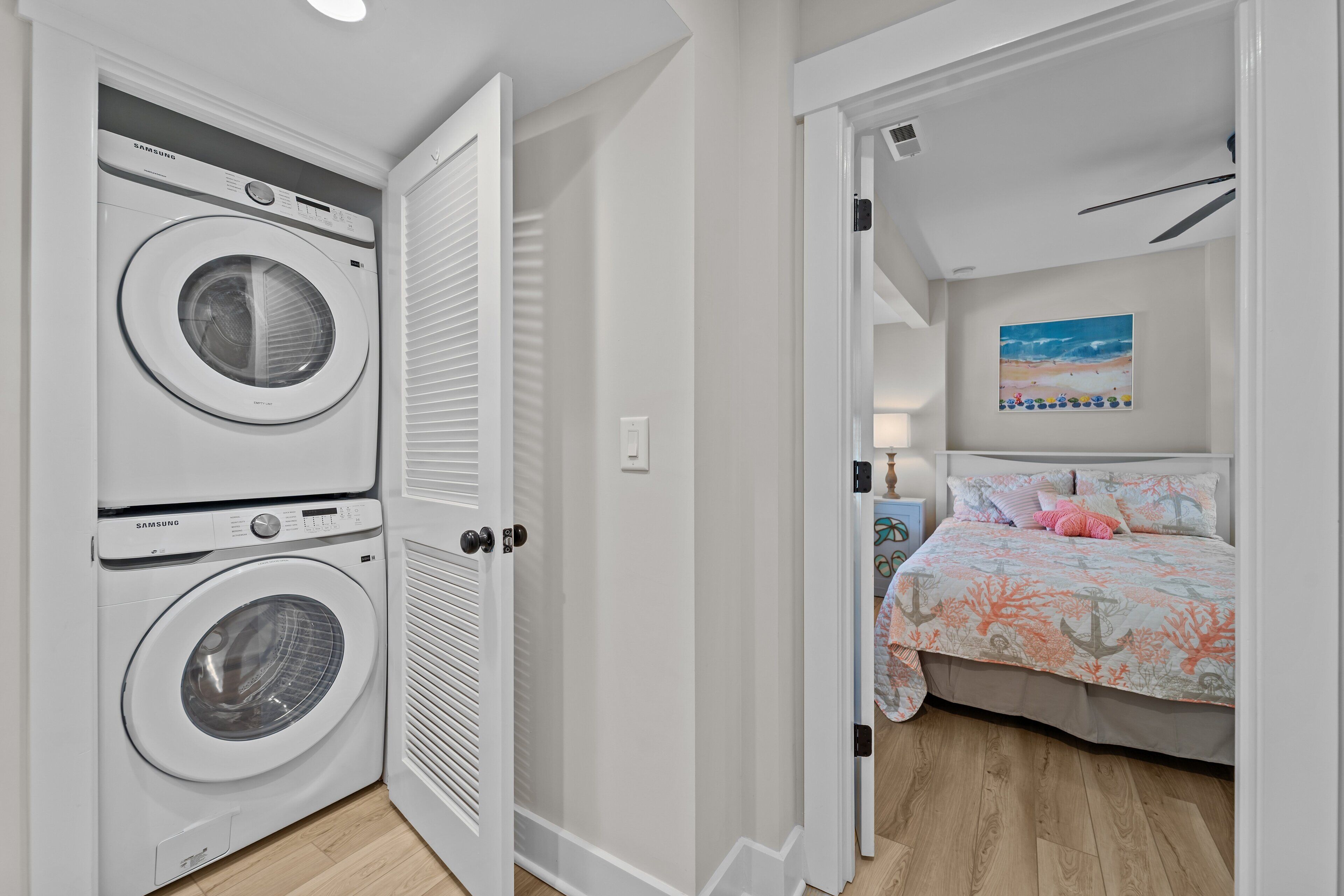 Une buanderie équipée de deux machines à laver superposées et une chambre à coucher avec un lit et un tableau au mur.
