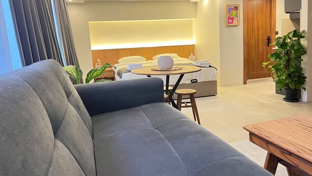 A modern hotel room with a sofa, a dining table, a bed with a headboard, a wooden door, and a potted plant. - Khalkedon Suites (Istanbul)