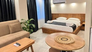 A hotel room with a bed, a sofa, a small table, a plant, and an air conditioning unit. - Khalkedon Suites (Istanbul)
