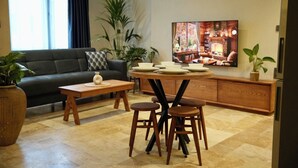 A living room with a sofa, a coffee table, a dining table with chairs, a TV, and potted plants. - Khalkedon Suites (Istanbul)