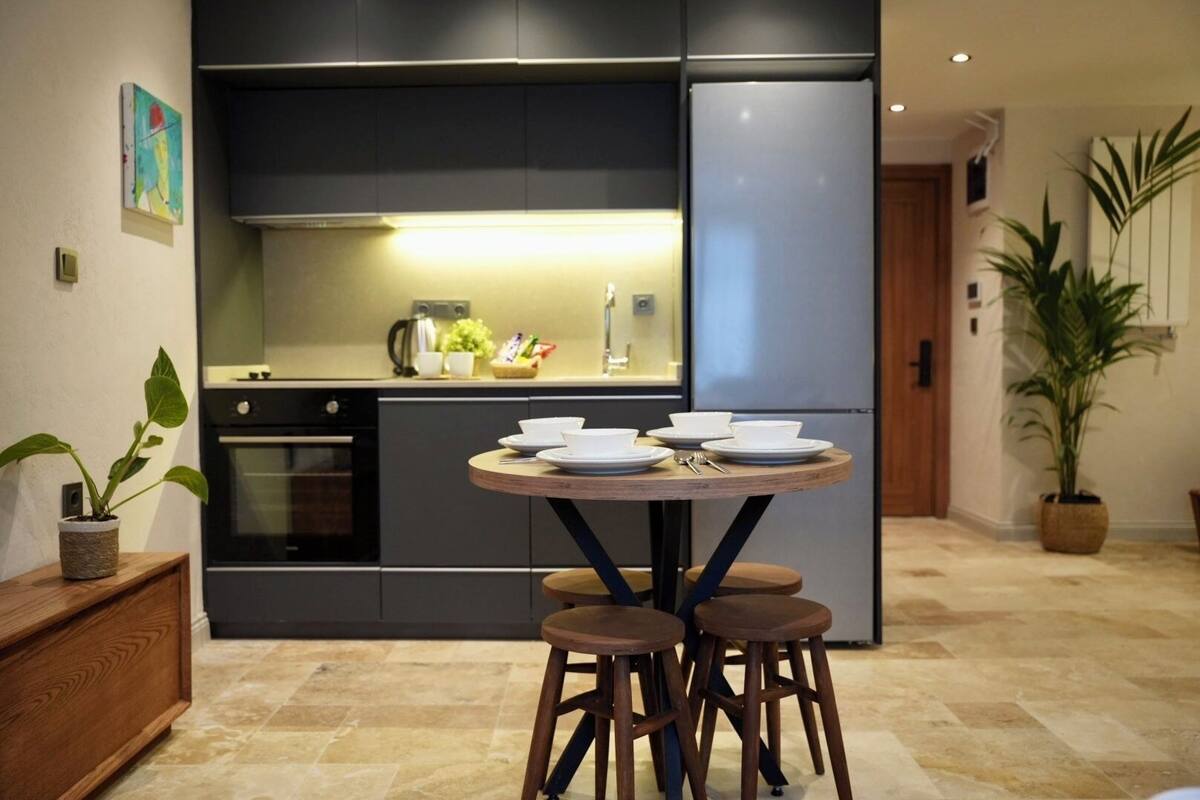 A modern kitchen with a central island, a refrigerator, and a dining area with stools.