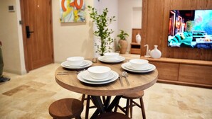 A dining area with a round wooden table set for six, surrounded by chairs. There is a television mounted on the wall displaying a scene from a show or movie. - Khalkedon Suites (Istanbul)